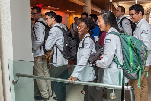 students in white coats and backpacks in the hallway